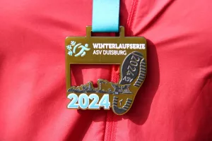 ahaufnahme der Medaille der Winterlaufserie ASV Duisburg 2024, präsentiert auf einem roten RWO Endurance Team Trikot.